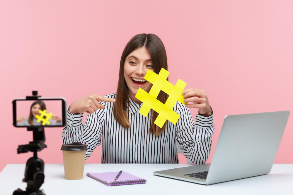 Garota segurando a hashtag enquanto fala em frente a uma câmera.